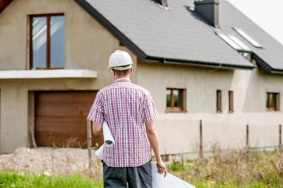 Profesional de reformas con unos planos frente a una vivienda antes de empezar la obra