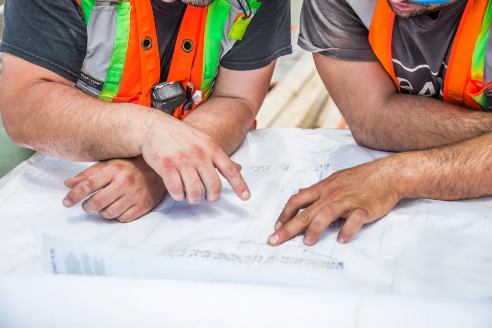 Dos personas revisando unos planos sobre una mesa, comparando un presupuesto